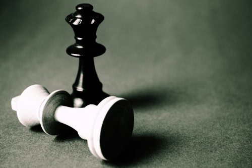 Black king standing over fallen white king on chessboard.