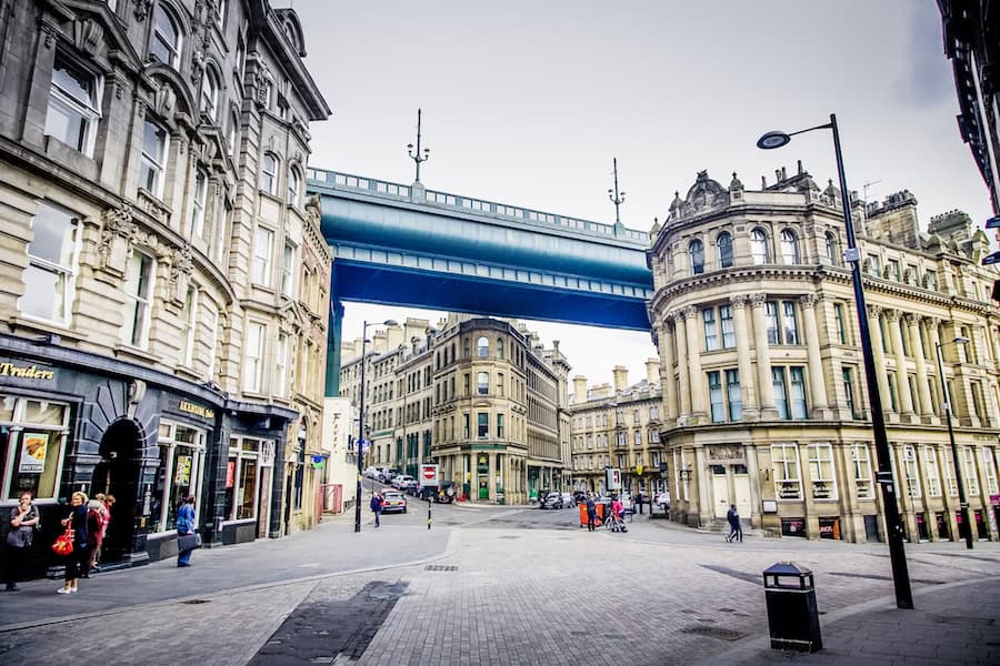 City street with historic buildings and a blue bridge overhead.