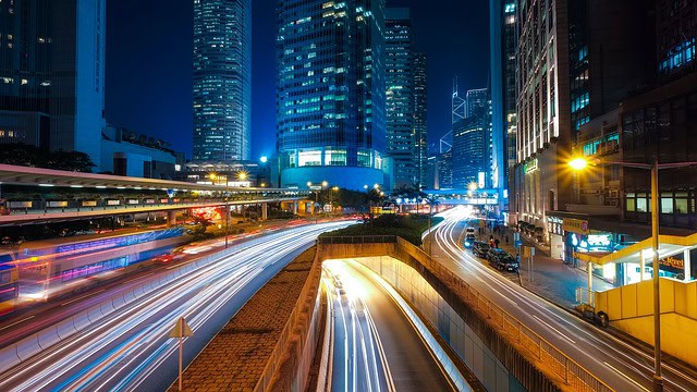 Urban city skyline with bright lights and fast-moving traffic at night.