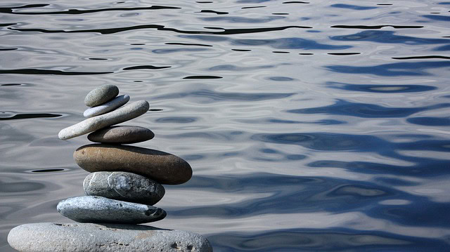 Stack of smooth stones balanced on a shoreline with water ripples in the background.